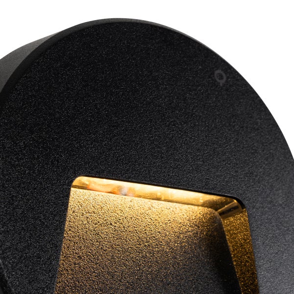 Runde Außenwandleuchte aus schwarzem Material mit strukturierter Oberfläche und warmem Lichtstrahl.
