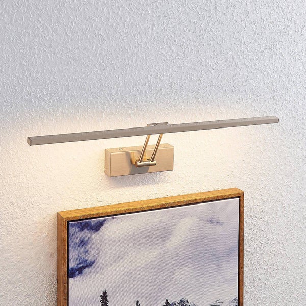 Moderne LED-Bilderleuchte aus Metall, die ein gerahmtes Gemälde an einer weißen Wand mit Putzstruktur beleuchtet.