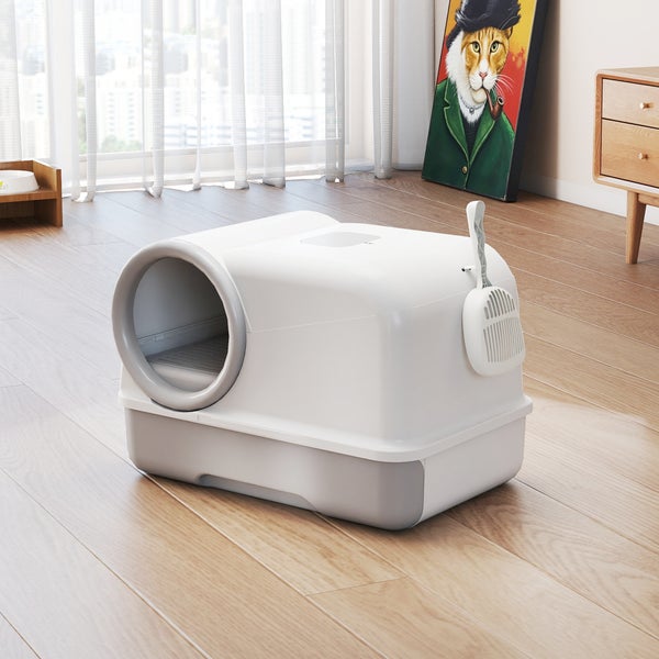 Geschlossene Katzentoilette aus Kunststoff mit Streuschaufel in einem hellen, modern eingerichteten Zimmer mit Holzboden.