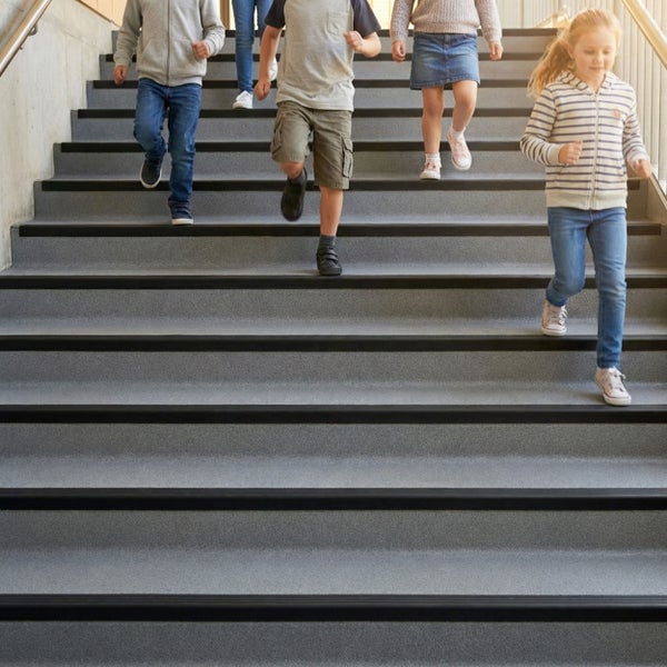 Gruppe von Kindern läuft eine Treppe mit rutschfestem Belag und schwarzen Stufenkanten im Innenbereich herab.