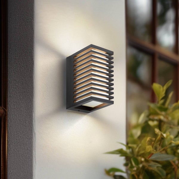 Moderne schwarze Außenwandleuchte mit horizontalen Lamellen und warmem Lichtstrahl auf einer weißen Wand.
