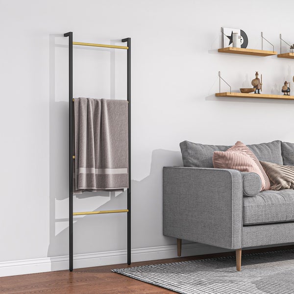 Schwarze Handtuchleiter mit Holzsprossen und grauem Handtuch an einer Wand in einem hellen, modernen Wohnzimmer neben einem grauen Sofa.