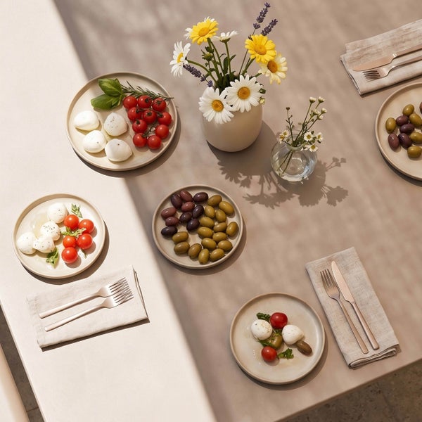 Gedeckter Tisch mit Vorspeisentellern, Besteck auf Leinenservietten und Blumenvasen in hellem Ambiente.