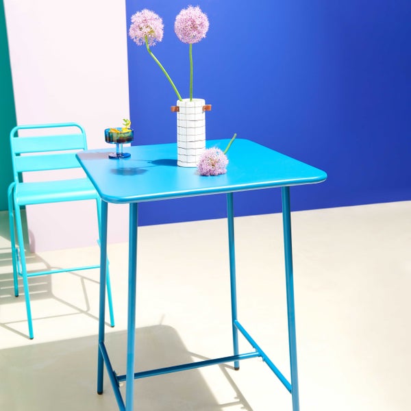 Blauer Bartisch aus Metall mit Barstuhl, weißer Vase mit lila Blumen und Cocktailglas in einer hellen, modern gestalteten Umgebung.