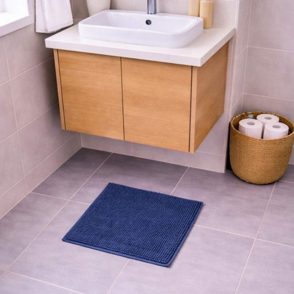Blaue quadratische Badematte in einem hellen Badezimmer mit hängendem Holz-Waschtischunterschrank und weißem Aufsatzwaschbecken.