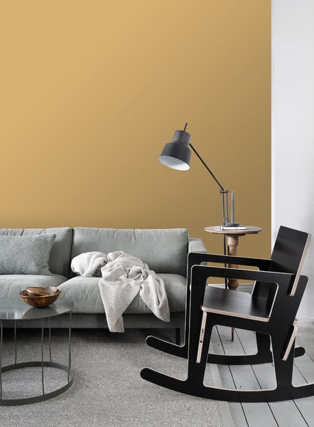 Wohnzimmer mit grauem Sofa, Beistelltisch, Stehlampe und Schaukelstuhl vor ockerfarbener Wand