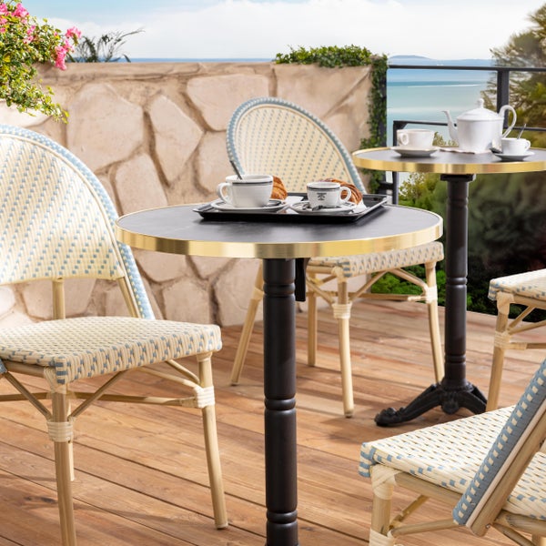 Bistro-Set auf einer Holzterrasse mit runden Tischen mit Goldrand und geflochtenen Bistrostühlen im französischen Stil.