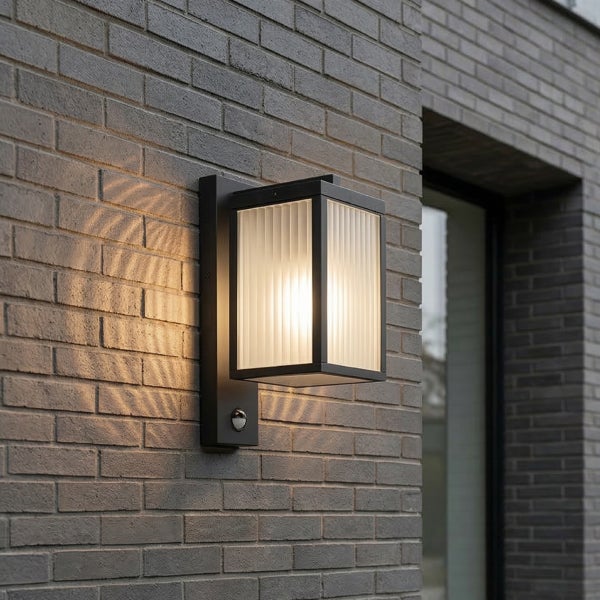 Moderne Außenwandleuchte in Rechteckform mit Bewegungsmelder und geriffeltem Glas an einer Ziegelwand.