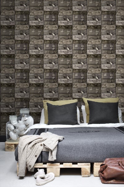 Schlafzimmer mit Tapete im Vintage-Koffer-Design, Bett aus Paletten und dekorativen Glühbirnen in einem Glasgefäß.