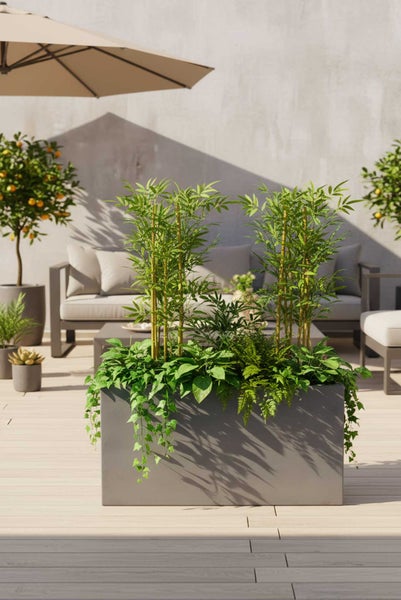 Moderne Dachterrasse mit grauer Lounge-Ecke, großen Pflanzgefäßen und Stadtblick.