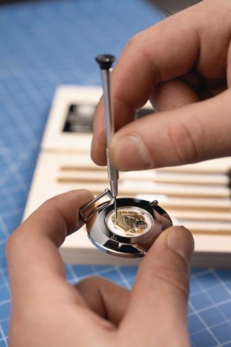 Nahaufnahme von Händen, die mit einem Schraubendreher an einer Uhr arbeiten