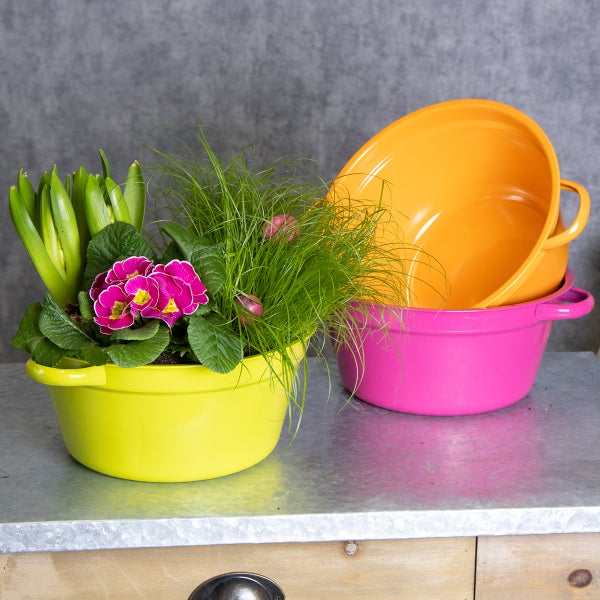 Arrangement aus Primeln und Gräsern in gelbem Pflanzgefäß, daneben gestapelte Pflanzgefäße