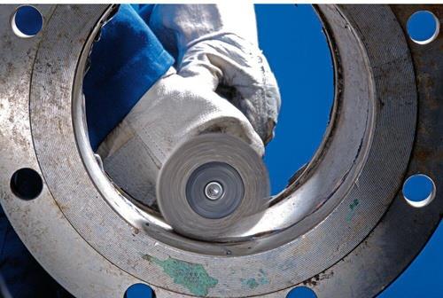 Ein Arbeiter reinigt eine Metallflanschverbindung mit einer Schleifscheibe.