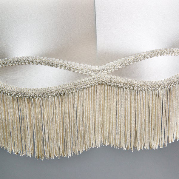 Lampenschirm-Detail mit Satin-Stoff, geflochtener Zierborte und langen Fransen.
