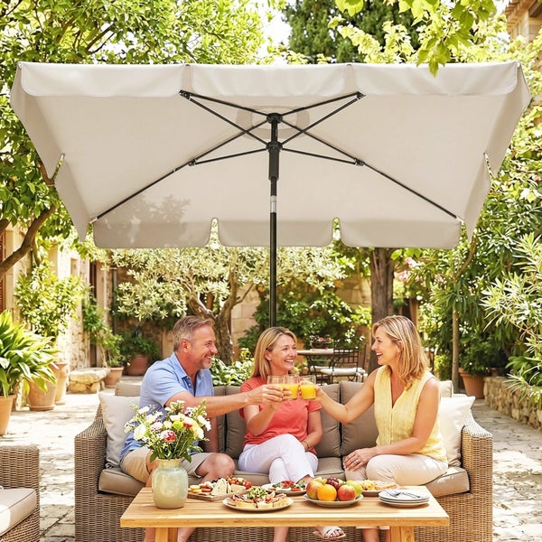 Drei Personen sitzen auf einem Garten-Loungesofa unter einem großen, rechteckigen hellbeigen Sonnenschirm in einer hellen Gartenanlage.