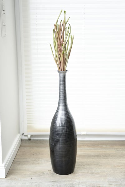 Hohe, schlanke Bodenvase mit feiner horizontaler Struktur und dekorativen Kunstzweigen in einem hellen Raum.