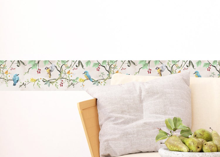 Selbstklebende Tapetenbordüre mit Vogel- und Pflanzenmotiv an einer Wand hinter einem Sofa.