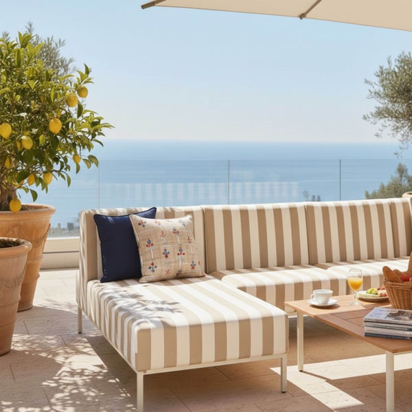 Gestreifte Gartenlounge mit Kissen, Holztisch und Zitronenbaum auf einer hellen Terrasse mit Meerblick.