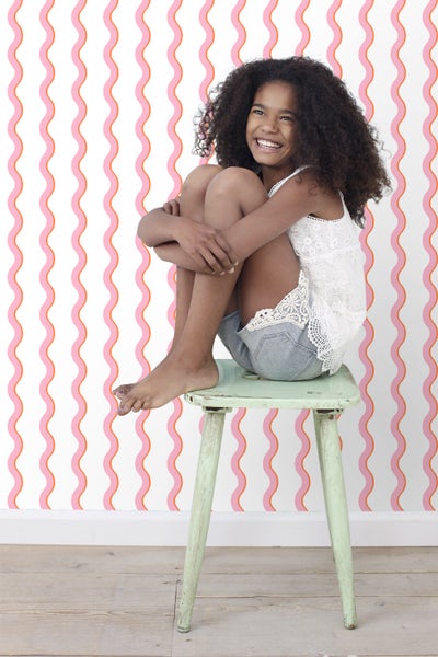Mädchen sitzt auf einem Hocker vor einer Wand mit Wellenmuster