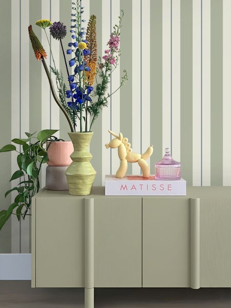 Gestreifte Tapete in Creme, Salbeigrün und Blau hinter einem Sideboard mit Vasen und Blumen.