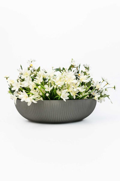 Künstliche weiße Blumen in einer grauen, ovalen Pflanzschale mit Rillenstruktur.
