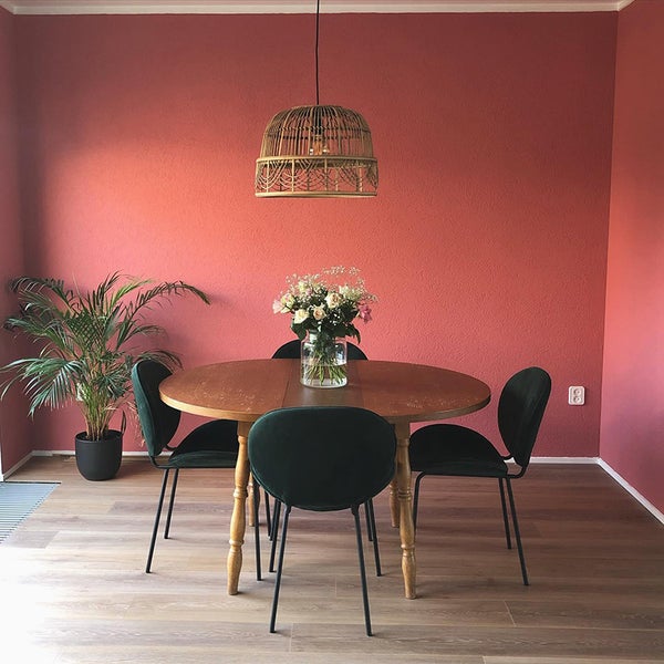Esszimmer mit rundem Holztisch, vier Stühlen, Blumenvase, Pendelleuchte und Zimmerpflanze