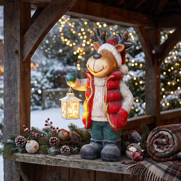 Weihnachtsdekoration Rentierfigur mit Laterne auf einem Holzuntergrund dekoriert mit Tannenzweigen und Weihnachtskugeln im Außenbereich
