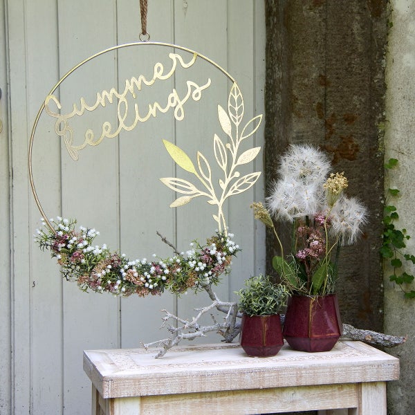 Dekorative Sommer-Szene mit Blumenkranz, Schriftzug Sommer Feelings und Dekoration auf einem Beistelltisch.