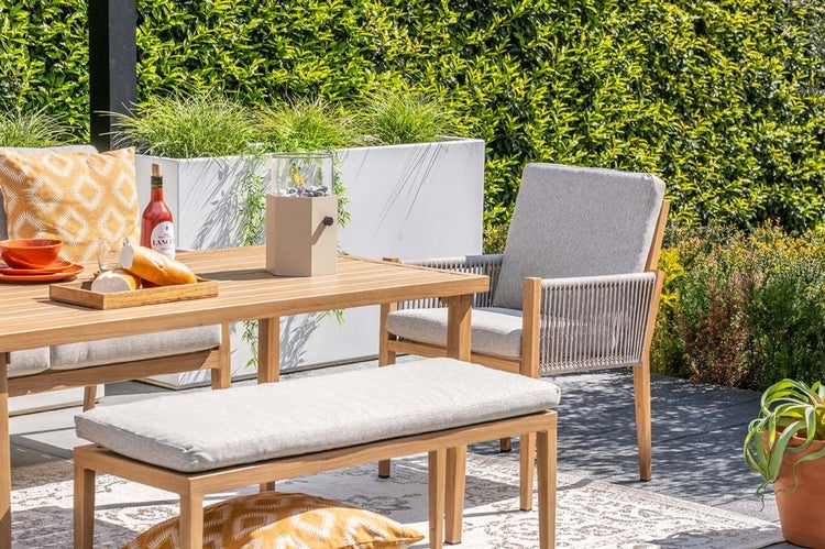 Gartenmöbelset aus Holz mit Esstisch, Bank und Sessel mit Seilbespannung auf einer Terrasse mit Hecke.