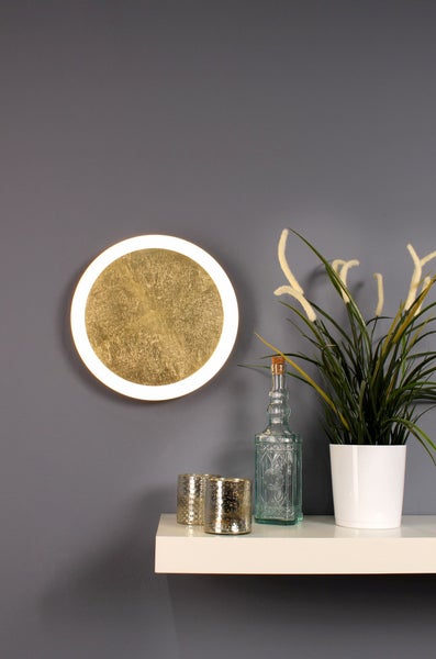 Runde LED-Wandleuchte mit strukturierter goldfarbener Oberfläche und weißem Leuchtring über einem weißen Regal mit dekorativen Gegenständen.