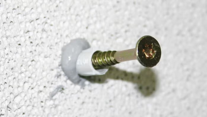 Eine Schraube wird in einen Dübel mit Dichtmasse in eine Wand aus Polystyrol eingesetzt.