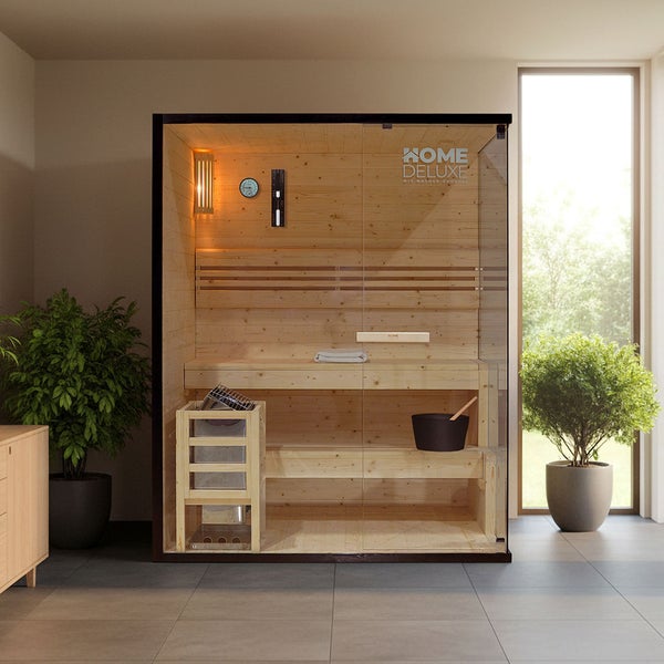 Moderne Heimsauna aus Holz mit Glastür, Innenbeleuchtung, Saunaofen und Zubehör in einem hellen, gut beleuchteten Raum mit Pflanzen.