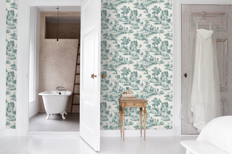 Helles Zimmer mit Vliestapete im Toile-de-Jouy-Stil, Blick auf eine freistehende Badewanne und einen Beistelltisch aus Holz.