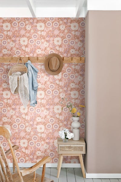 Vliestapete mit floralem Retromuster in Rosa und Weiß in einem hellen Zimmer mit Holzmöbeln und Garderobe.
