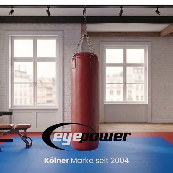 Boxsack in einem hellen Fitnessraum mit weißen Backsteinwänden, großen Fenstern und blauer Bodenmatte. eyepower Logo.
