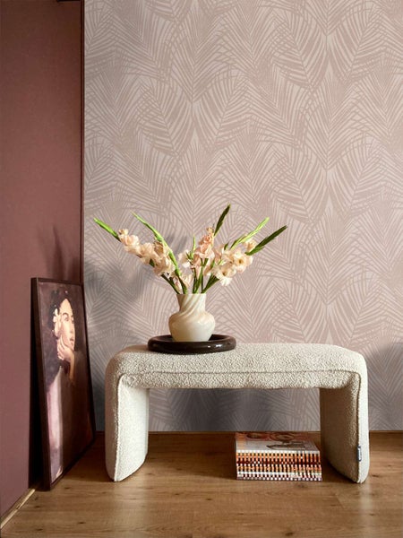 Moderne Vliestapete mit Palmenblattmuster vor einer Wohnzimmerwand, kombiniert mit einem texturierten Hocker und einer Blumenvase.