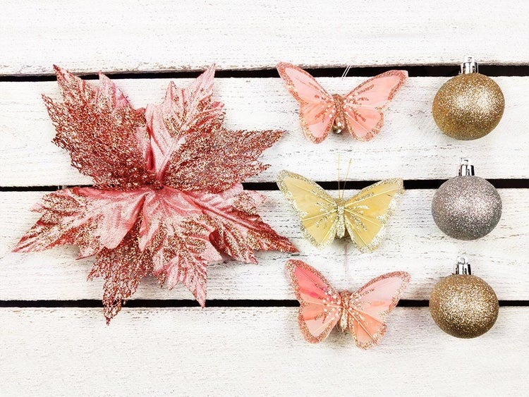 Weihnachtsbaumschmuck Set bestehend aus künstlicher Poinsettie, drei Schmetterlingen und drei Weihnachtskugeln mit Glitzer auf weißem Holz.