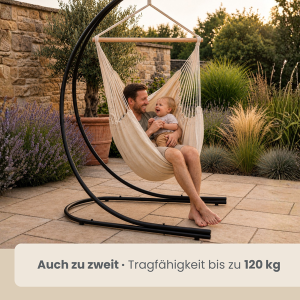 Ein Mann sitzt mit seinem Kind in einem Hängesessel mit Metallgestell auf einer Terrasse im Garten. Tragfähigkeit bis zu 120 Kilogramm.