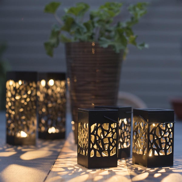 Mehrere dekorative schwarze Laternen mit Ausschnitten auf einem Tisch mit Pflanze