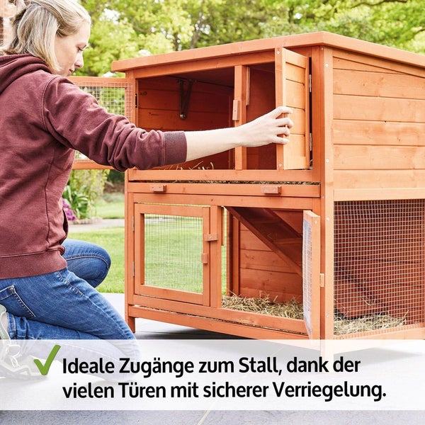 Person öffnet eine Tür eines zweistöckigen Kleintierstalls aus Holz. Der Stall verfügt über mehrere sicher verriegelbare Türen für einfachen Zugang.