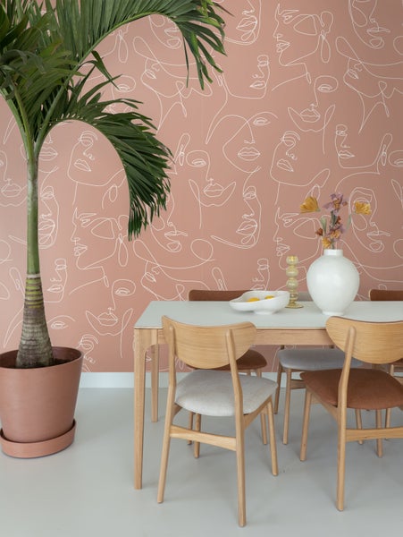 Esszimmer mit Esstisch, Stühlen, Zimmerpflanze und Wandtapete mit Gesichtsmuster