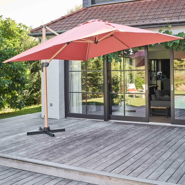 Moderner Ampelschirm in Terracotta auf einer Holzterrasse vor einem Haus mit großen Glasschiebetüren und Garten.