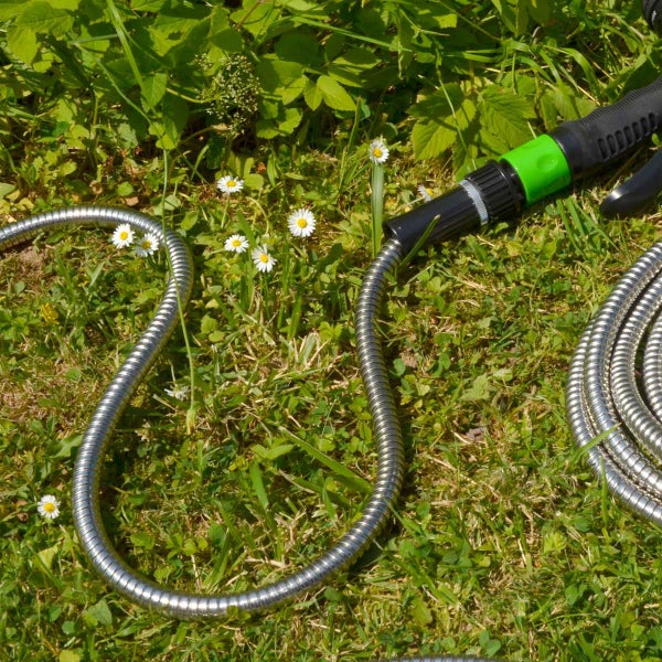 Flexibler Gartenschlauch aus Edelstahl mit Spritzdüse auf einer Rasenfläche mit Gänseblümchen.