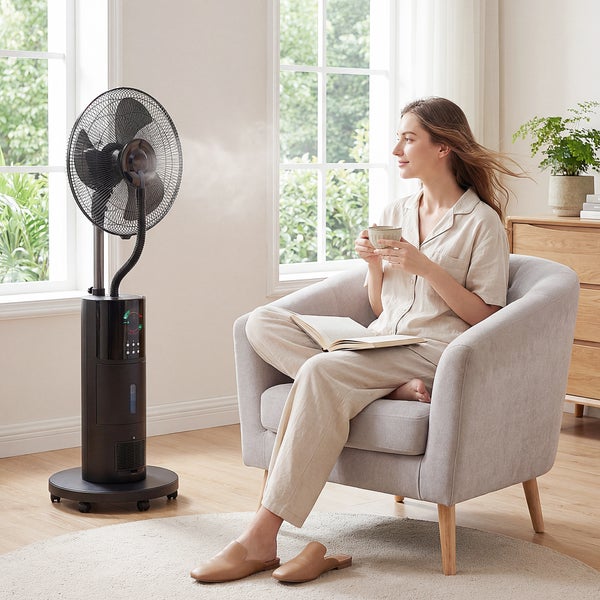 Schwarzer Standventilator mit Sprühnebelfunktion in einem hellen Wohnzimmer. Moderner Ventilator mit Wassertank neben einem Sessel.