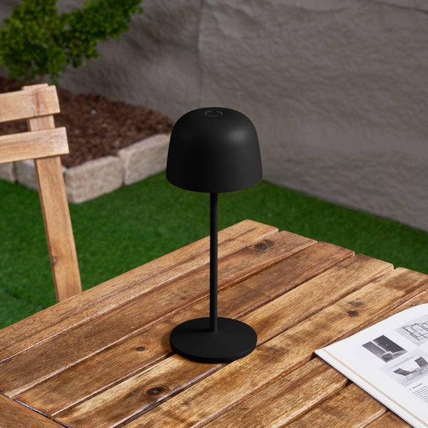 Schwarze LED-Außen-Tischleuchte in Pilzform auf einem hölzernen Gartentisch im Außenbereich.