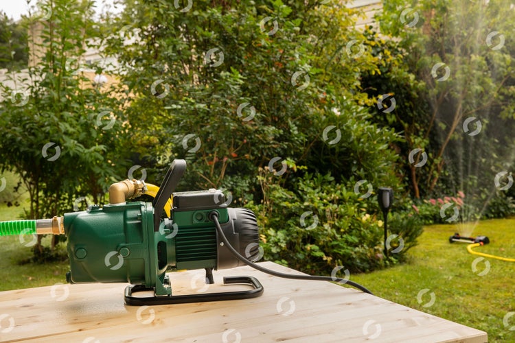 Gartenpumpe auf Holztisch mit Rasensprenger im Hintergrund
