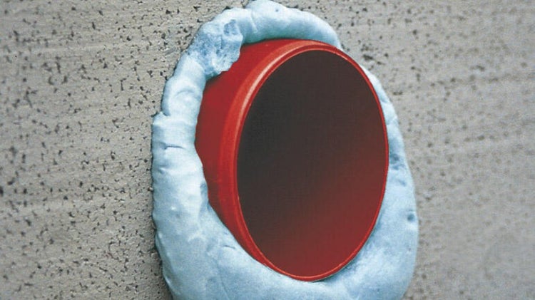 Rotes Rohr, abgedichtet mit Bauschaum, in einer Betonwand