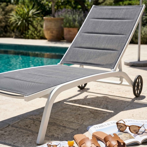 Weiße Gartenliege mit Rollen am Pool, gepolsterte graue Liegefläche aus Textilgewebe, Gestell aus Aluminium.