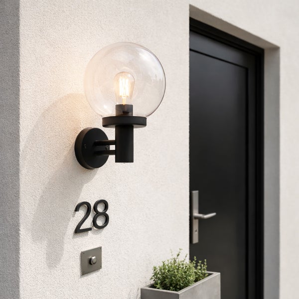 Moderne Außenwandleuchte mit transparenter Glaskugel und schwarzer Halterung, montiert an einer weißen Hauswand neben einer schwarzen Haustür.