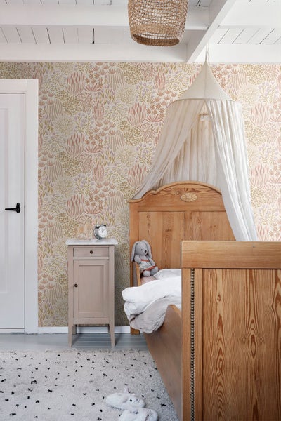 Helle Kinderzimmer-Szene mit floraler Tapete in Erdtönen, einem Holzbett mit Baldachin und einem rustikalen Nachttisch.